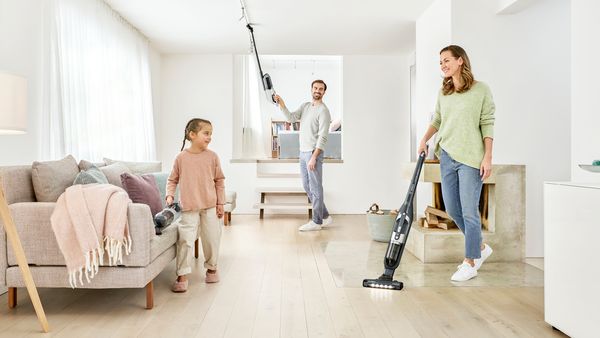 A family of three use a 2in1 vacuum at different levels and on different surfaces in a bright living area.