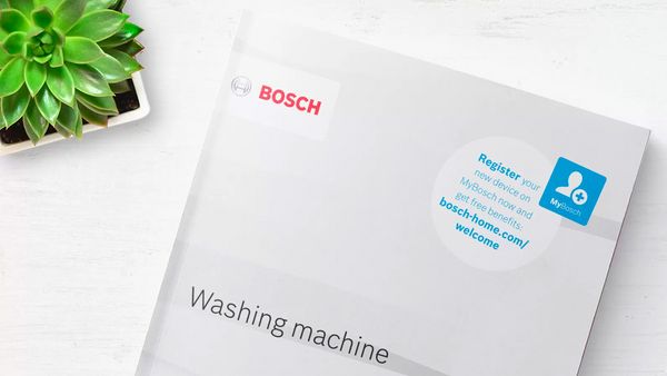 Eine Anleitung für eine Bosch Waschmaschine liegt neben einer Sukkulente auf einem weißen Tisch. 