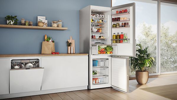 Ein Smartphone zeigt den Inhalt einer Kühl-Gefrier-Kombination mit der Home Connect App. Im Hintergrund ist die geöffnete Kühl-Gefrier-Kombination in der Küche sichtbar und gibt den Blick frei auf komfortables und modernes Lebensmittelmanagement.