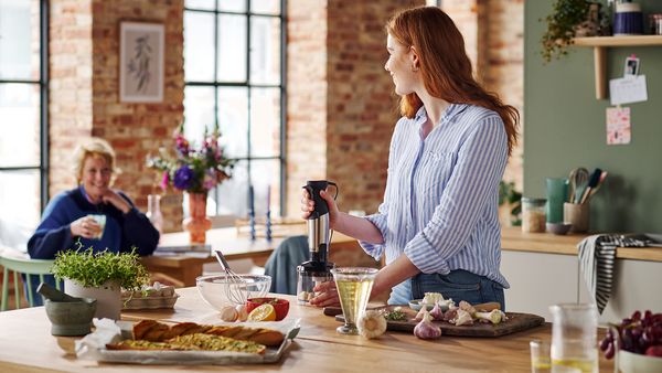Eine Frau steht in der Küche und bereitet Knoblauchbaguette zu. Mit dem ErgoMaster Serie 6 von Bosch hackt sie die Knoblauchzehen.
