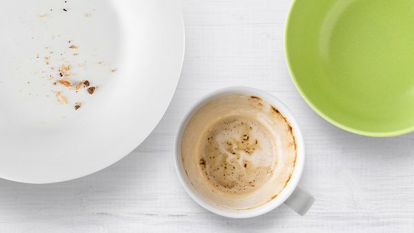 Ein grüner Teller, ein schmutziger weißer Teller und eine schmutzige Kaffeetasse vor einem weißen Hintergrund.