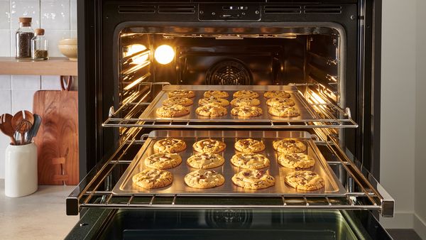 Zwei ausgezogene Schienen in einem Backofen zeigen Backbleche mit Cookies.