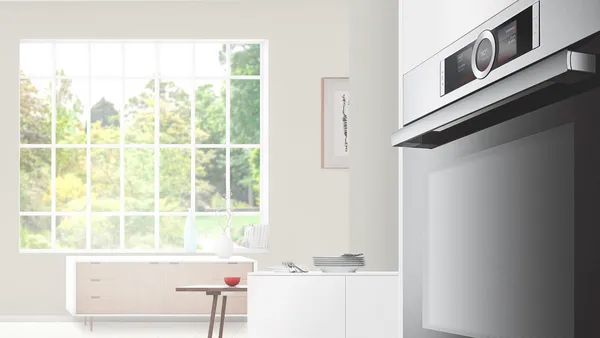 A built-in oven with a bright, modern living room in the background.