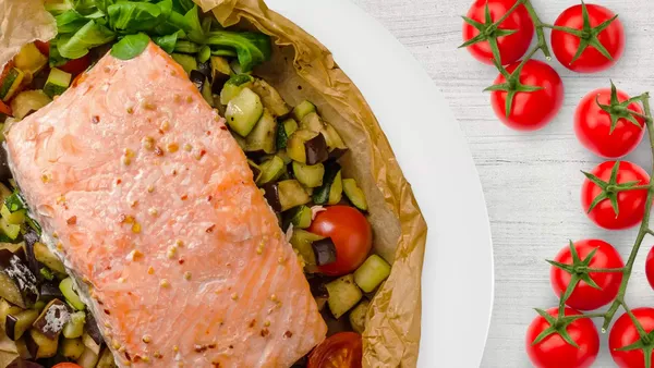 An opened oven bag reveals a delicious piece of salmon on a bed of vegetables.