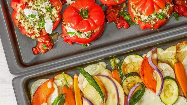 Two baking trays sit alongside each another – one with stuffed roasted peppers, the other with chopped roasted veg.