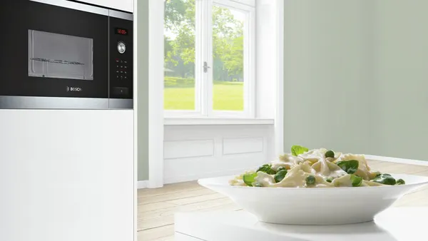 A freshly prepared pasta dish with herbs rests on a white counter with a built in oven in the background.