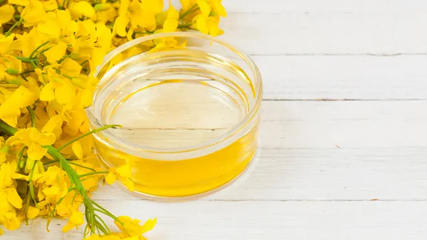 A wooden surface with a dish of oil next to yellow flowers.