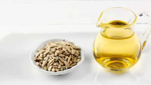 A small ceramic bowl of sunflower seeds stands next to a glass jug of oil.