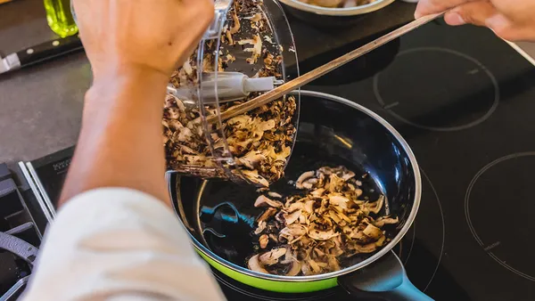 Someone scoops mushrooms from a glass bowl into a skillet.