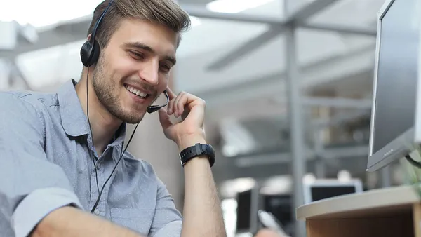 A friendly man wearing a headset and facing a computer screen takes a customer call.