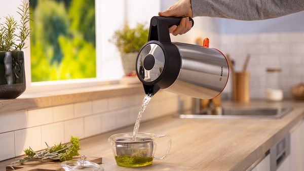 Voda se izlijeva iz MyMoment kuhala za vodu u staklenu šalicu s listićima čaja od metvice.