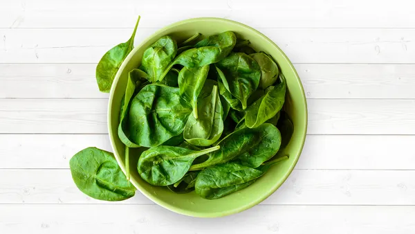 A green bowl of raw baby spinach leaves.