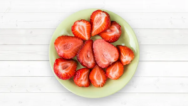 A green plate of halved strawberries.