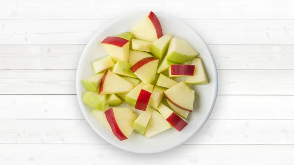 A white plate of chopped red and green apples.