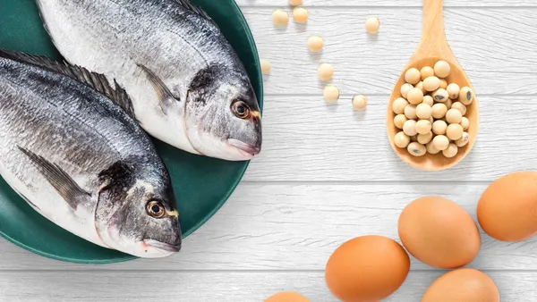 Two whole fishes on a teal plate alongside a ladle of beans and some eggs.