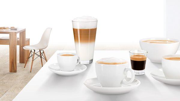 Mehrere Kaffeebecher und Gläser mit Kaffeespezialitäten, wie Espresso und Latte Macchiato, auf einer Arbeitsplatte.