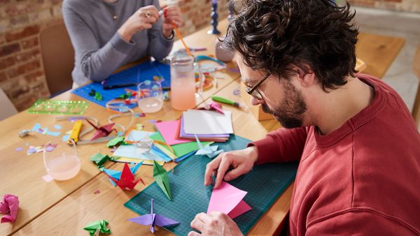 Zwei Personen sitzen gemeinsam an einem Tisch und widmen sich der Origamikunst.