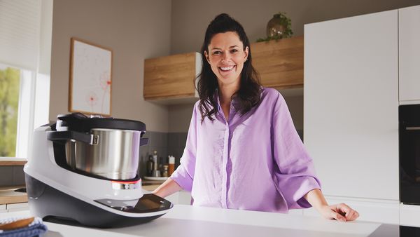 Eine Frau mit lächelndem Gesicht steht in einer modernen Küche neben einem Cookit.