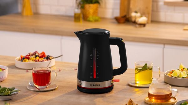 Bollitore Bosch nero su un tavolo, circondato da tazze di tè e frutta fresca, in un ambiente accogliente e luminoso.