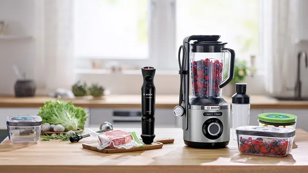 The VitaPower Series 8 blender filled with berries on a counter top. Next to it, a piece of steak in a sous vide bag.