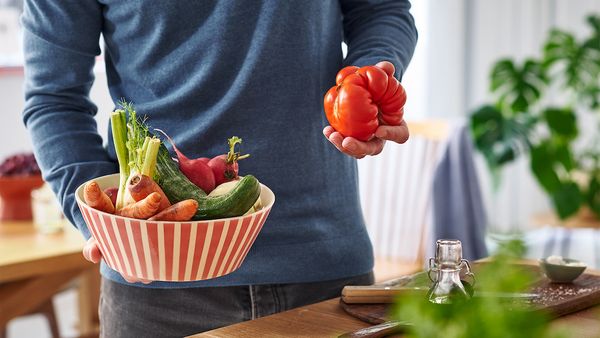 Ein Mann hält eine Schüssel voll Gemüse in der einen und eine Tomate in der anderen Hand.