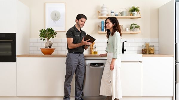 Cliente e técnico com um iPad a conversar numa cozinha em frente à máquina de lavar loiça.