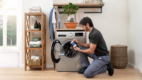 Technician with a cleaning product in his hand in front of a washing machine.