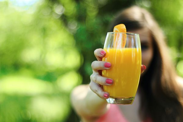 Młoda kobieta pokazuje szklankę z sokiem pomarańczowym przygotowanym w sokowirówce