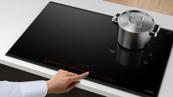 A person operating an electric cooktop with a stainless steel cooking pot.