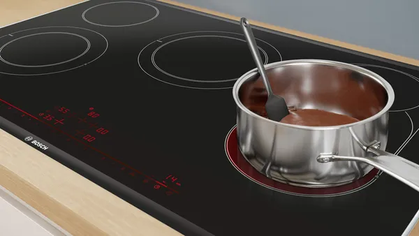 A stainless steel cooking pot with melting chocolate on an electric cooktop.