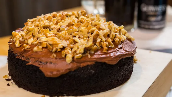 A delicious guinness and chocolate cake decorated with chopped nuts rests on a table. 