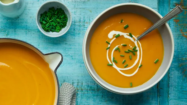 Bowls of roasted butternut pumpkin soup and small dish of chopped chives stand on a turquoise table.