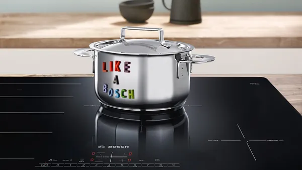 A stainless steel pot with letter magnets spelling &quot;like a bosch&quot; sits on an induction cooktop in a bright kitchen.