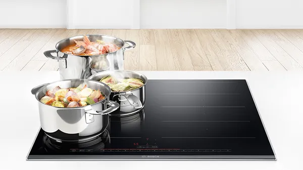 An induction cooktop with three consecutive pots with simmering vegetables on the left flex zone.