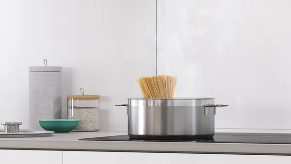 A stainless steel cooking pot with boiling water and protruding noodles on a ceramic cooktop.