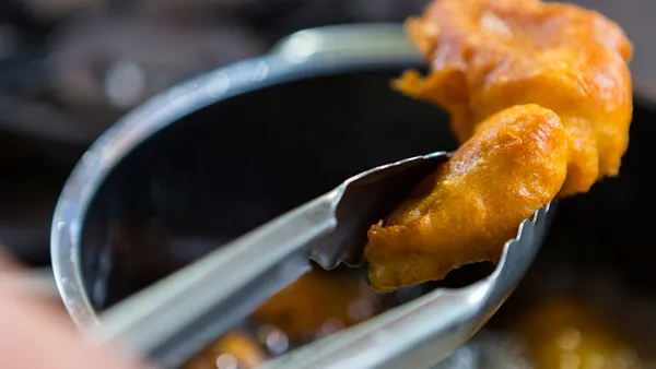 Tongs lifting something fried from a pot of oil.