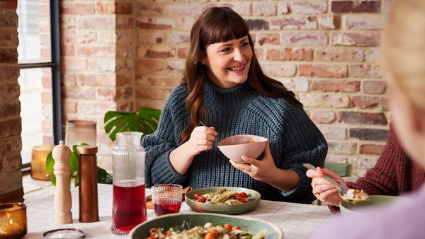 Eine Frau sitzt mit zwei weiteren Personen, die teilweise zu sehen sind, an einem Tisch und genießt leckere vegetarische Hausmannskost.