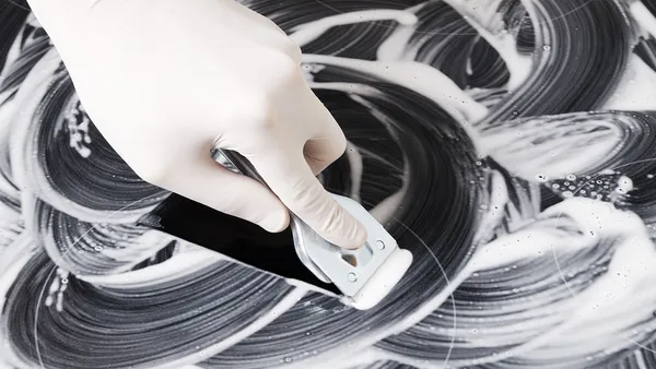 A ceramic cooktop rubbed with cleaning solution is being scraped with a ceramic cleaner.