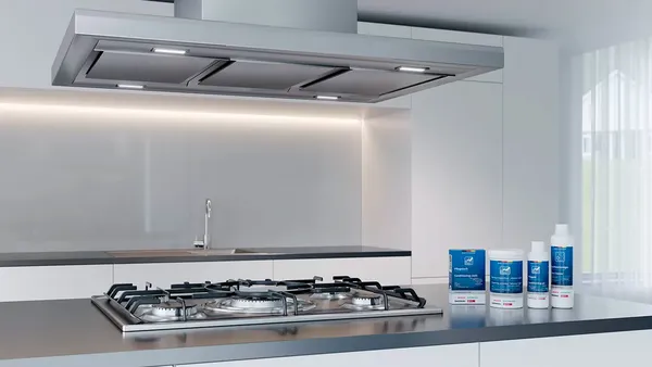 Stainless steel cleaning supplies next to a stainless steel gas stove, with a stainless steel island hood above.