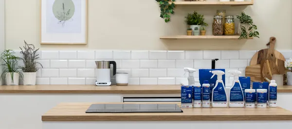 Cleaning utensils for kitchen appliances are placed on a kitchen island with a built-in ceramic cooktop. In the background, there is a bright, modern kitchen.