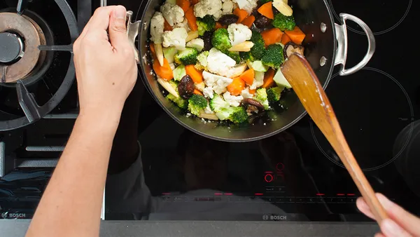 A person is stirring with a wooden cooking spoon in a saucepan.