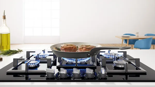 An induction cooktop with three consecutive pots with simmering vegetables on the left flex zone.