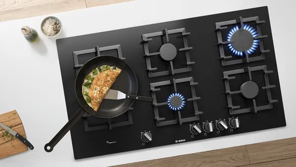 The top view of a gas stove with two burning flames and a pan with an omelette.