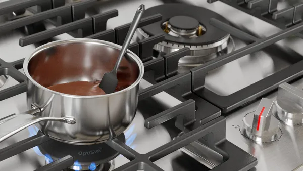 A stainless steel cooking pot with melting chocolate on a gas stove.