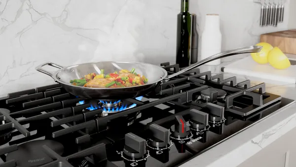 A gas stove with a pan containing meat and vegetables in a bright kitchen environment.