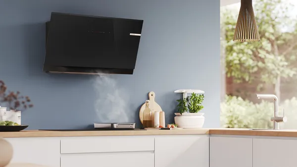 A black wall-mounted hood in a modern kitchen with blue walls is extracting steam from a roasting pan.