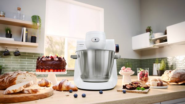 Robot kuchenny typu planetarnego Serie 6 w białej wersji na blacie kuchennym otoczony owocami i innymi produktami spożywczymi.