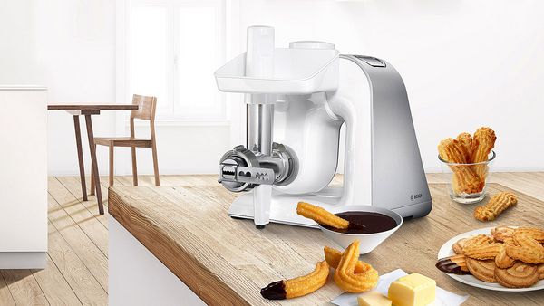 Bosch stand mixer with a whisk next to a cake and whipped cream.