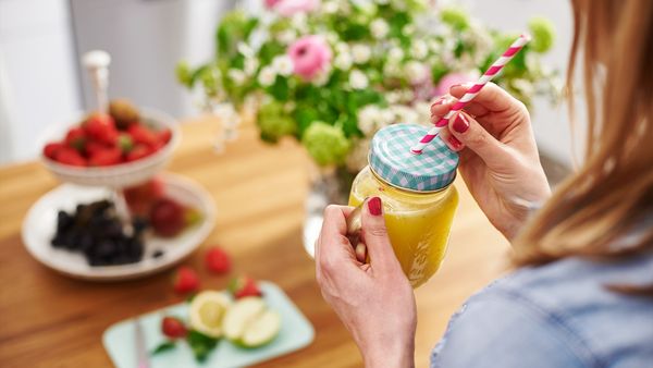 Eine Person hält einen frisch gepressten gelben Saft aus einer Bosch Küchenmaschine mit Entsafter in einem Trinkglas mit Strohhalm in der Hand.