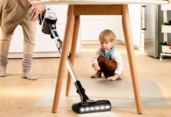 Person vacuuming mess under table with child watching
